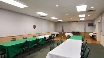 A conference room with long tables, green chairs, a flag, and a television on the wall.