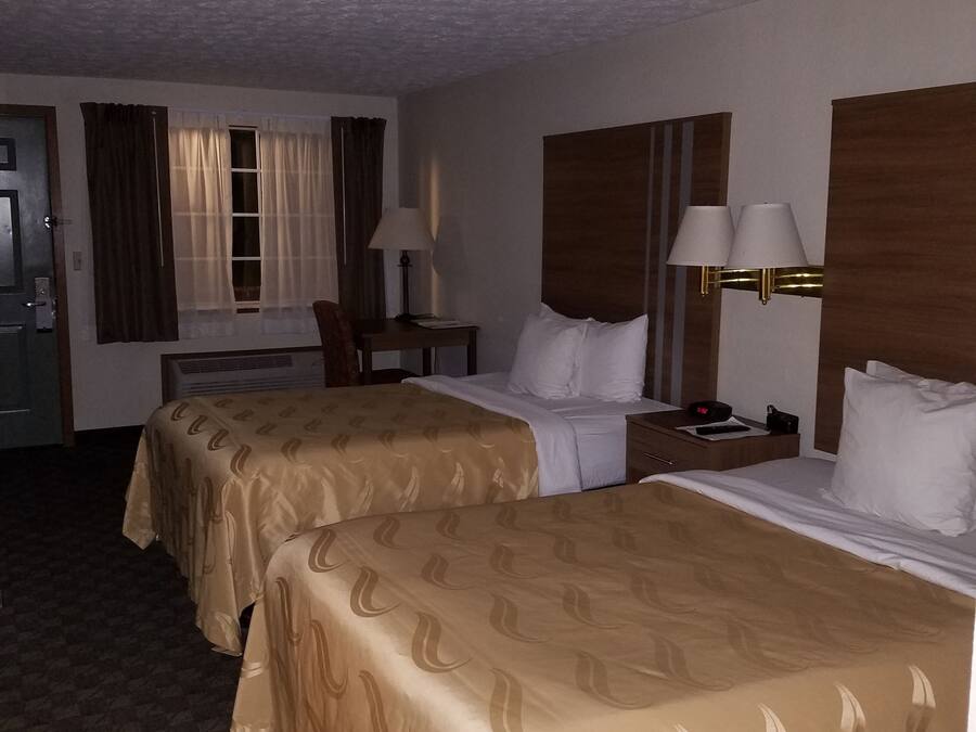 Ein Hotelzimmer mit zwei Betten, einem Schreibtisch, einem Stuhl, einer Lampe und einem Fenster mit Vorhängen.