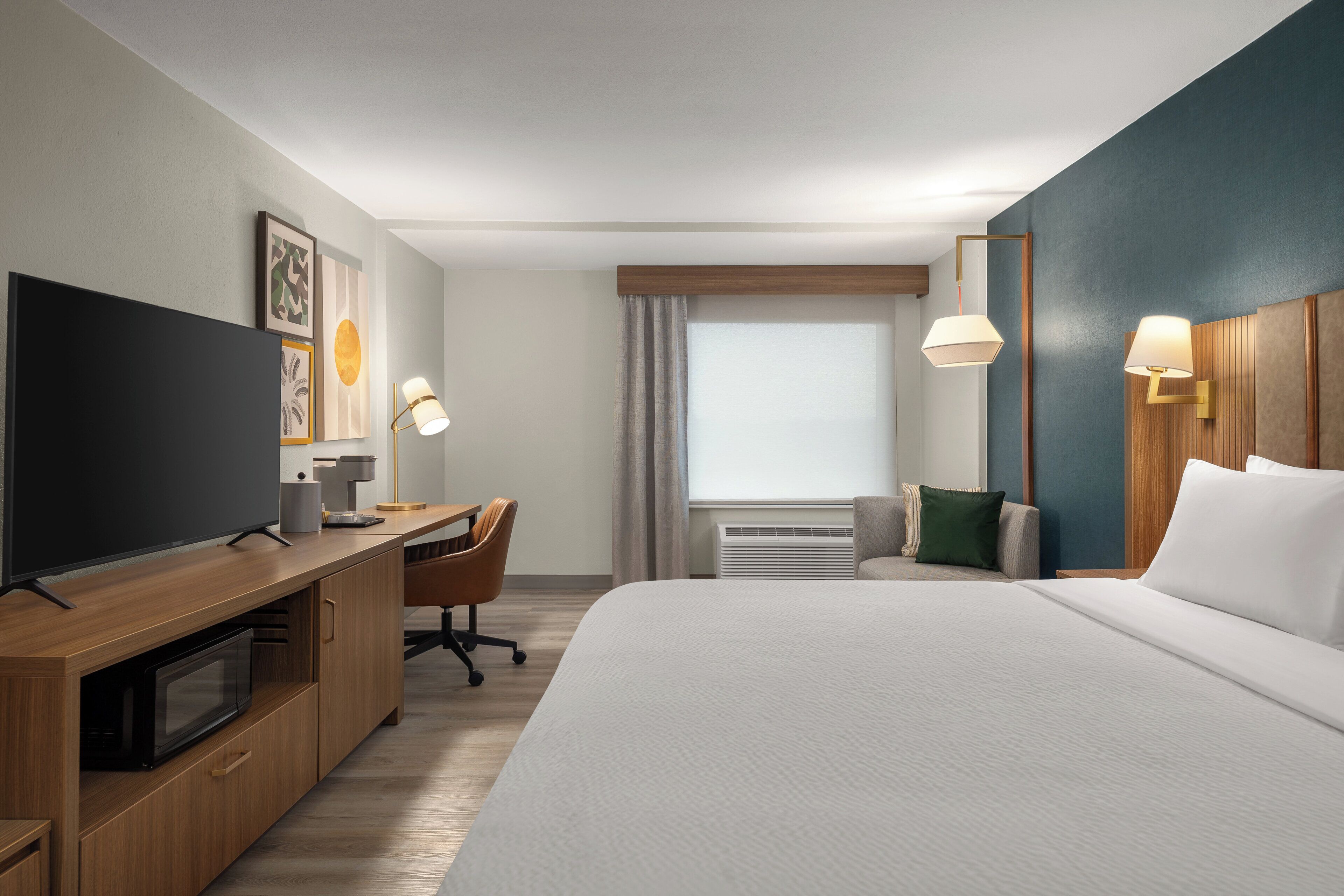 A hotel room with a bed, a desk, a television, and a window with curtains.