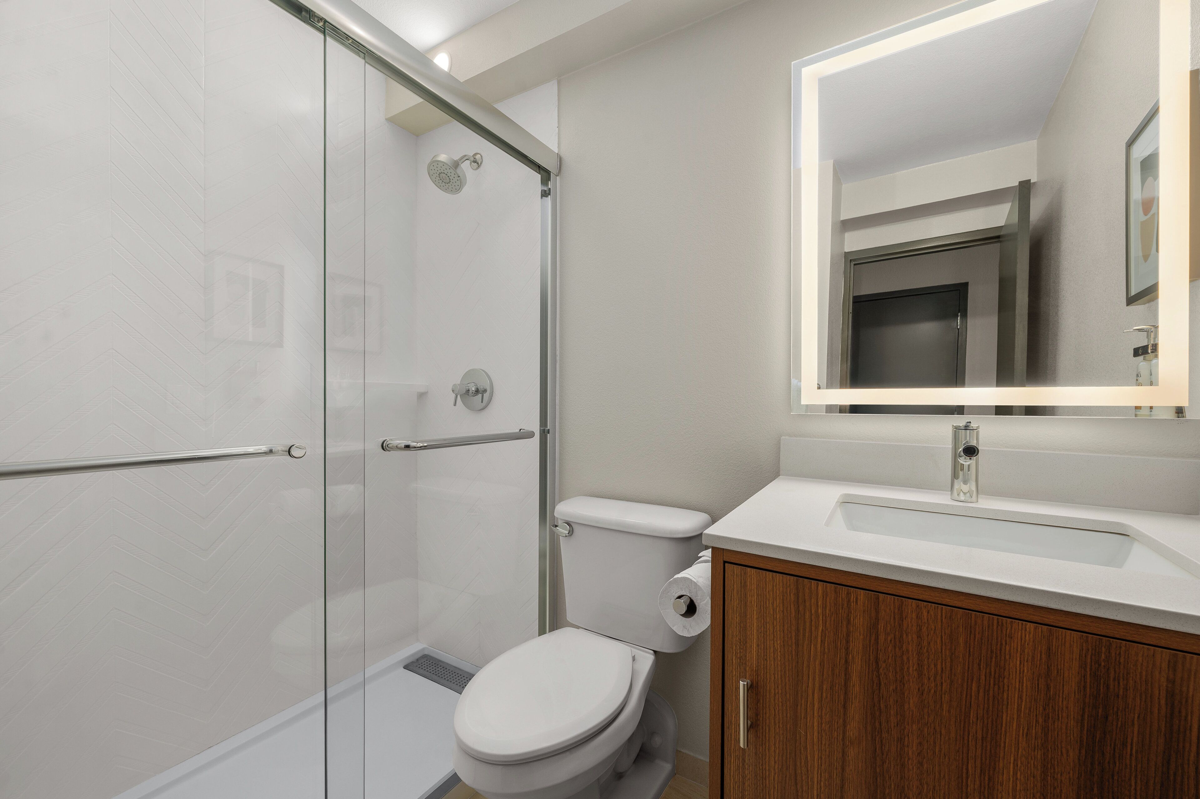 A modern bathroom with a glass shower enclosure, a toilet, a sink with a mirror above it, and wooden cabinetry.