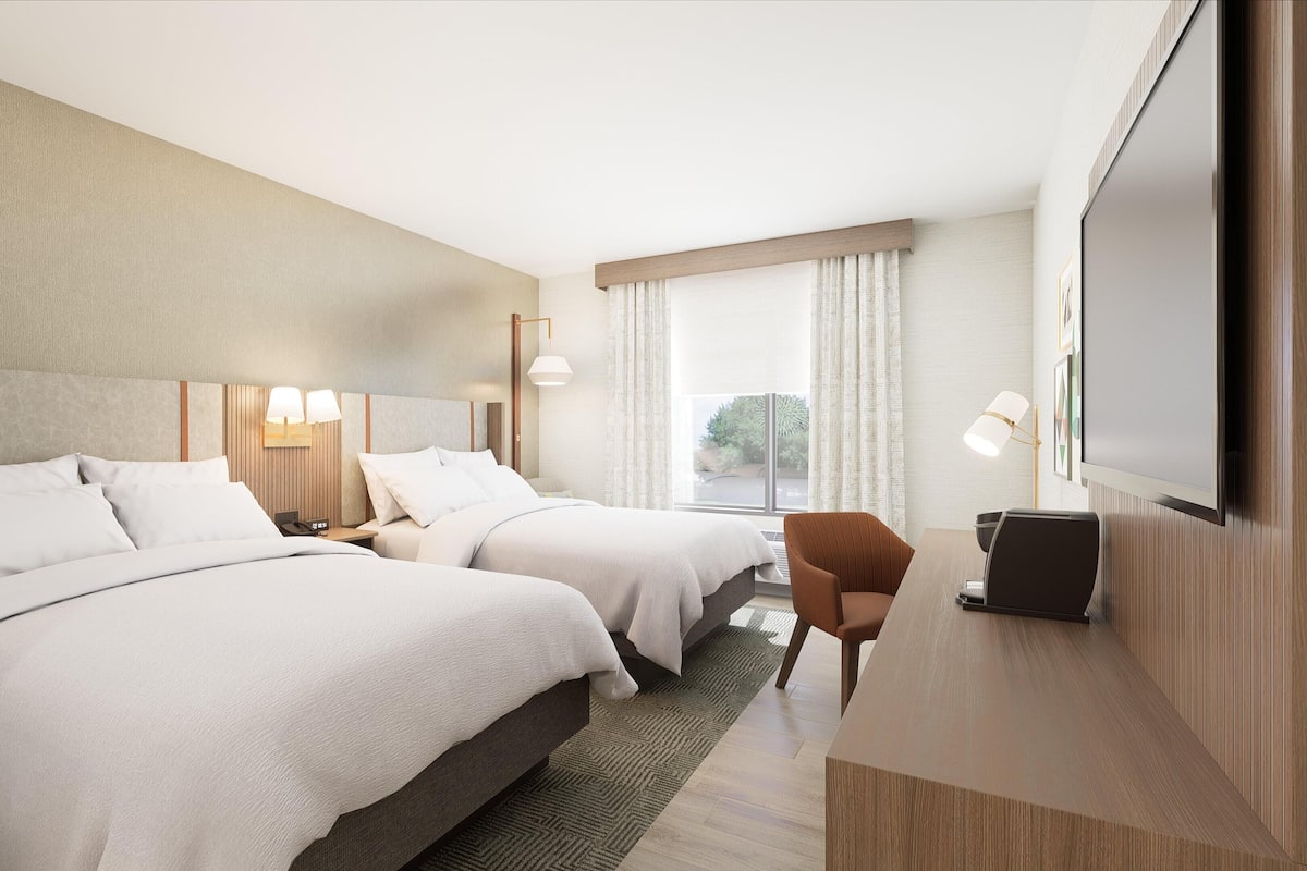 A hotel room with two beds, a desk, a chair, a TV, and a window with curtains.