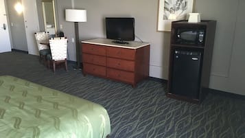 A hotel room with a bed, a dresser, a television, a microwave, and a framed picture on the wall.