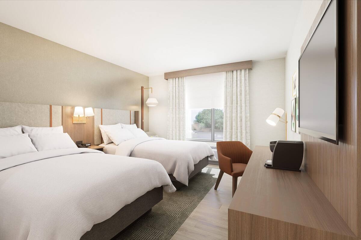 A hotel room with two beds, a desk, a chair, a TV, and a window with curtains.