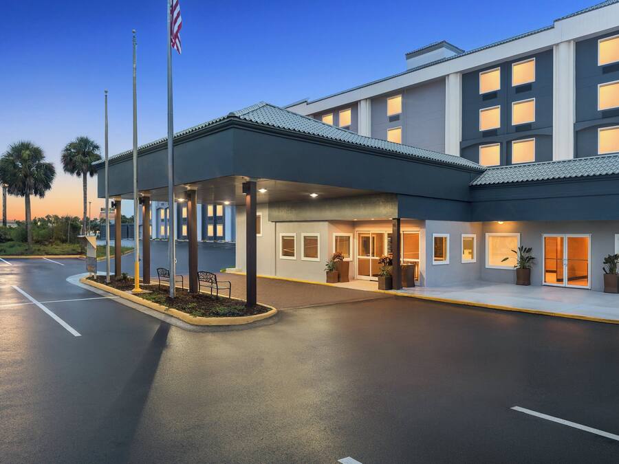 A modern hotel entrance with a covered waiting area, palm trees, and an American flag.