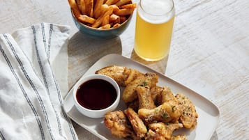 Un piatto di alette di pollo fritte, una ciotola di patatine fritte, un bicchiere di birra e una piccola ciotola di salsa.