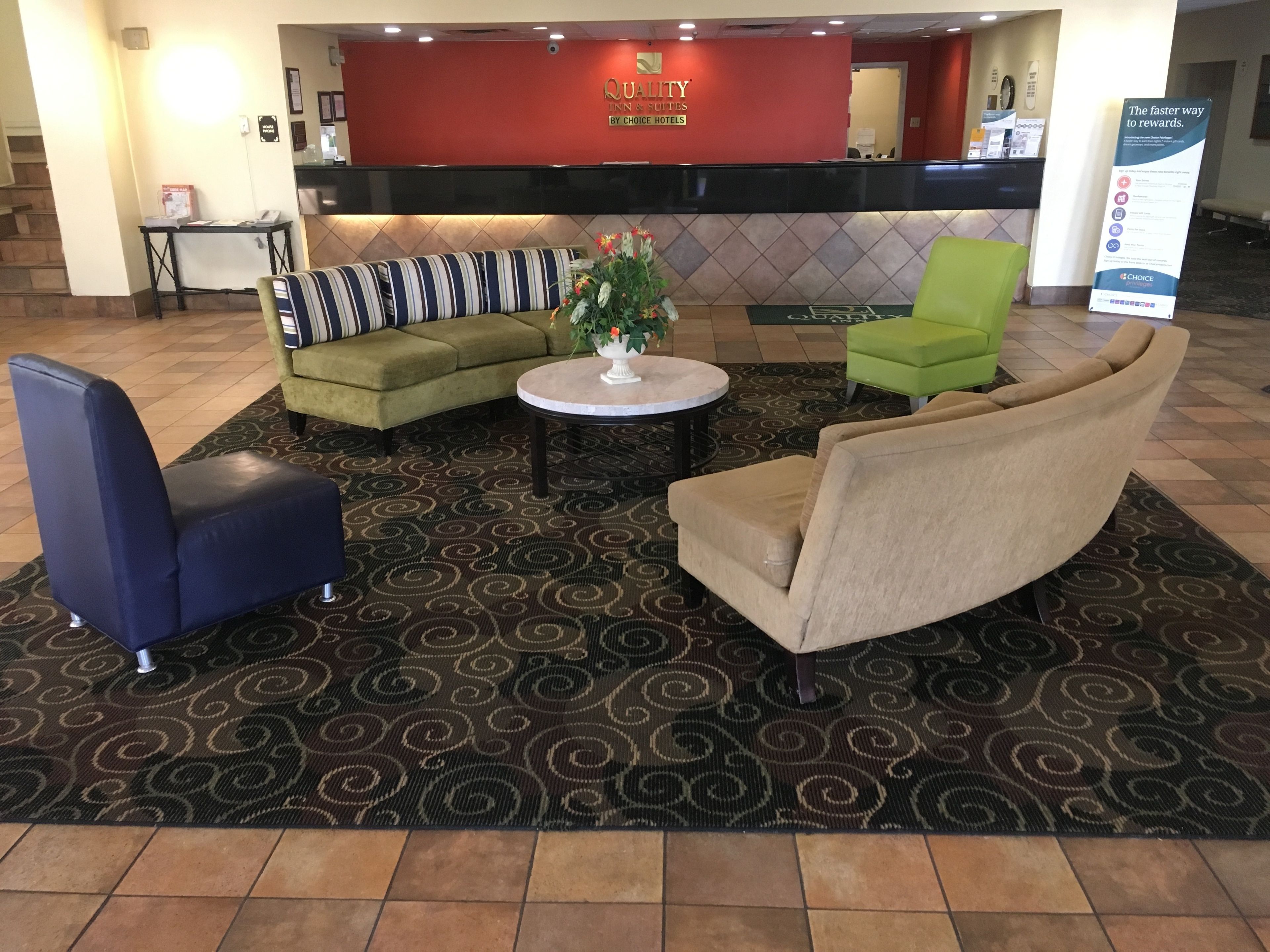 A hotel reception area with a reception desk, a sofa, a chair, and a small table with a vase of flowers.