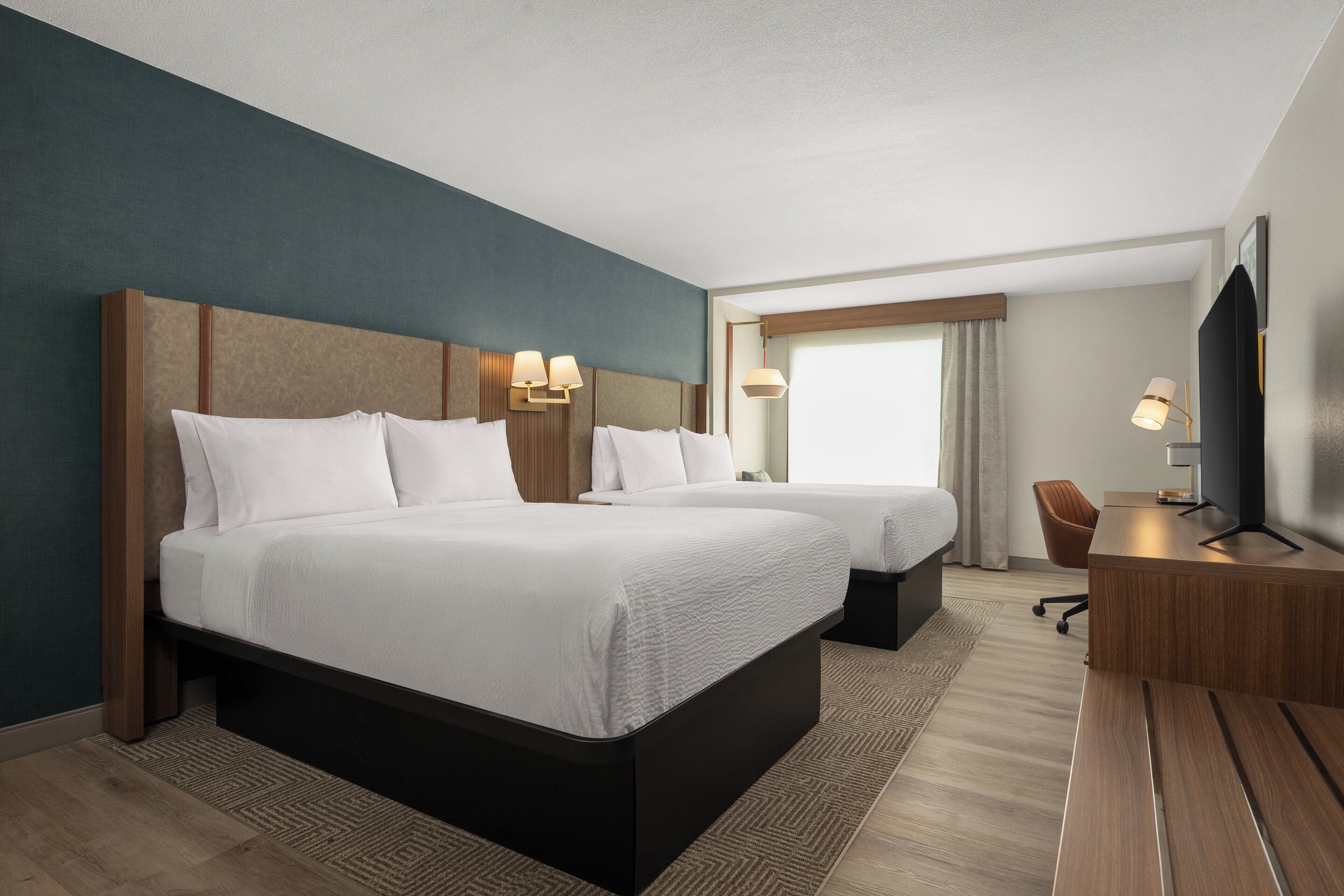 Habitación de hotel con dos camas, un escritorio, una silla y un televisor.