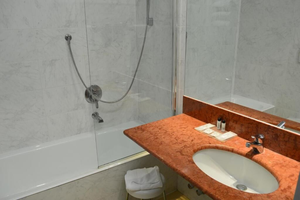 A modern bathroom with a glass-enclosed shower, a marble sink, and a vanity with toiletries.