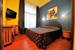 Una camera da letto con un letto, una scrivania, una sedia, un televisore e una lampada a parete.