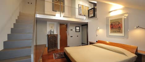 A bedroom with a large bed, a staircase, and a loft area with artwork.