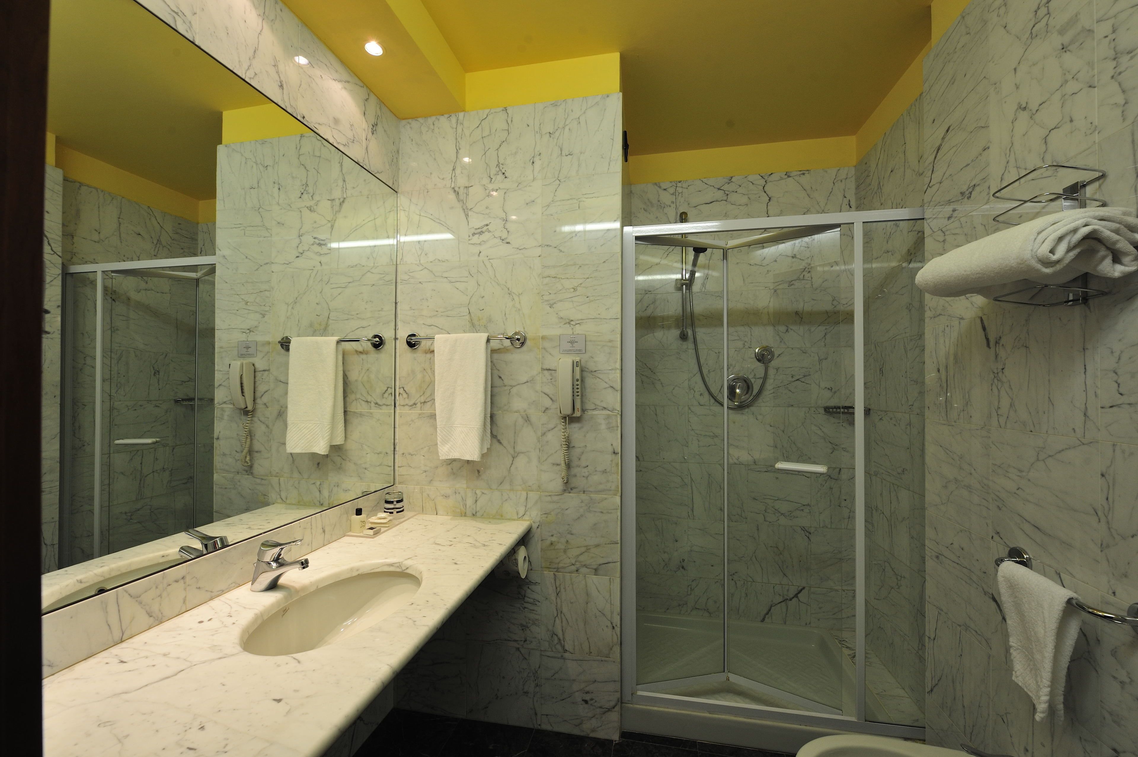 A modern bathroom with a marble sink, a glass-enclosed shower, and yellow walls.