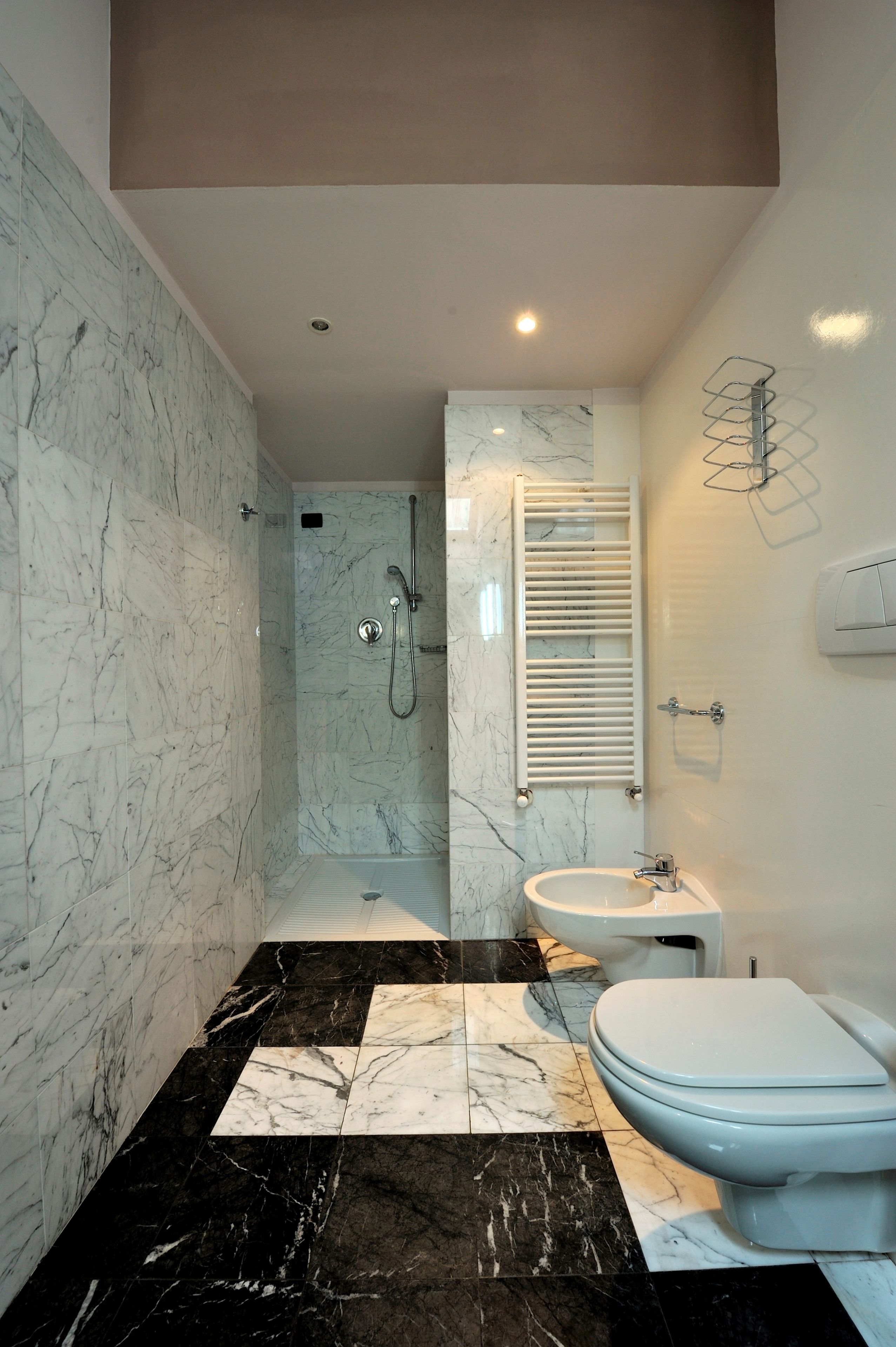Ein modernes Badezimmer mit Dusche, Toilette und Waschbecken, mit Marmorwänden und schwarz-weißen Fliesen.