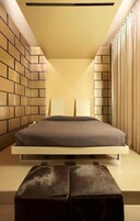 Camera da letto moderna con un letto al centro su una piattaforma, affiancato da pareti con motivo a mattoni e un'ampia finestra con tende.