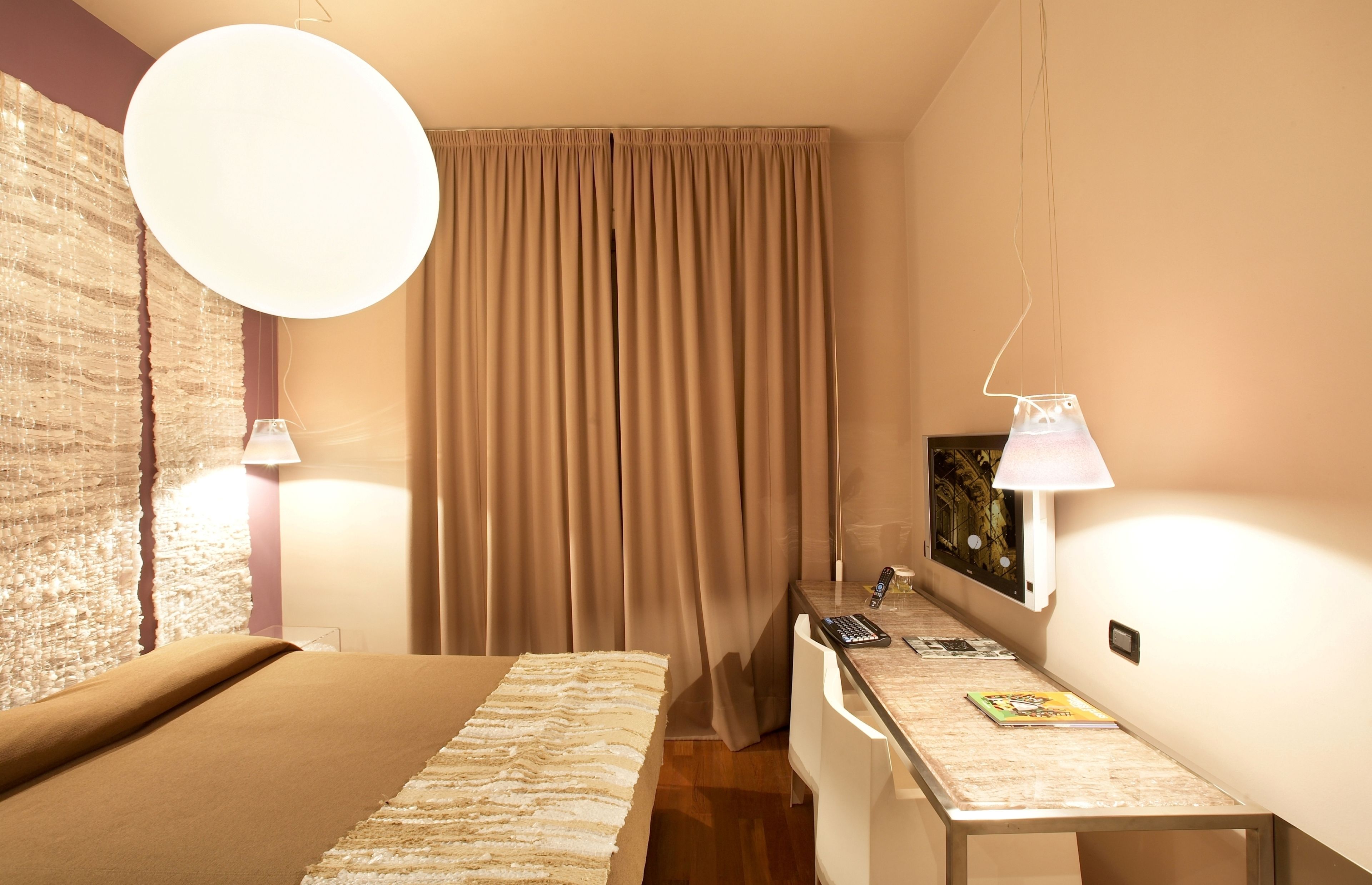 A hotel room with a bed, a desk with a lamp, a chair, a curtain, and a wall-mounted picture.