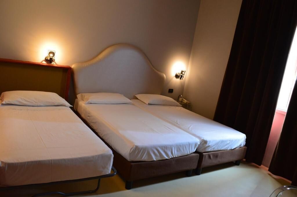 Une chambre avec deux lits simples, une tête de lit en bois, des lampes de chevet et un rideau.