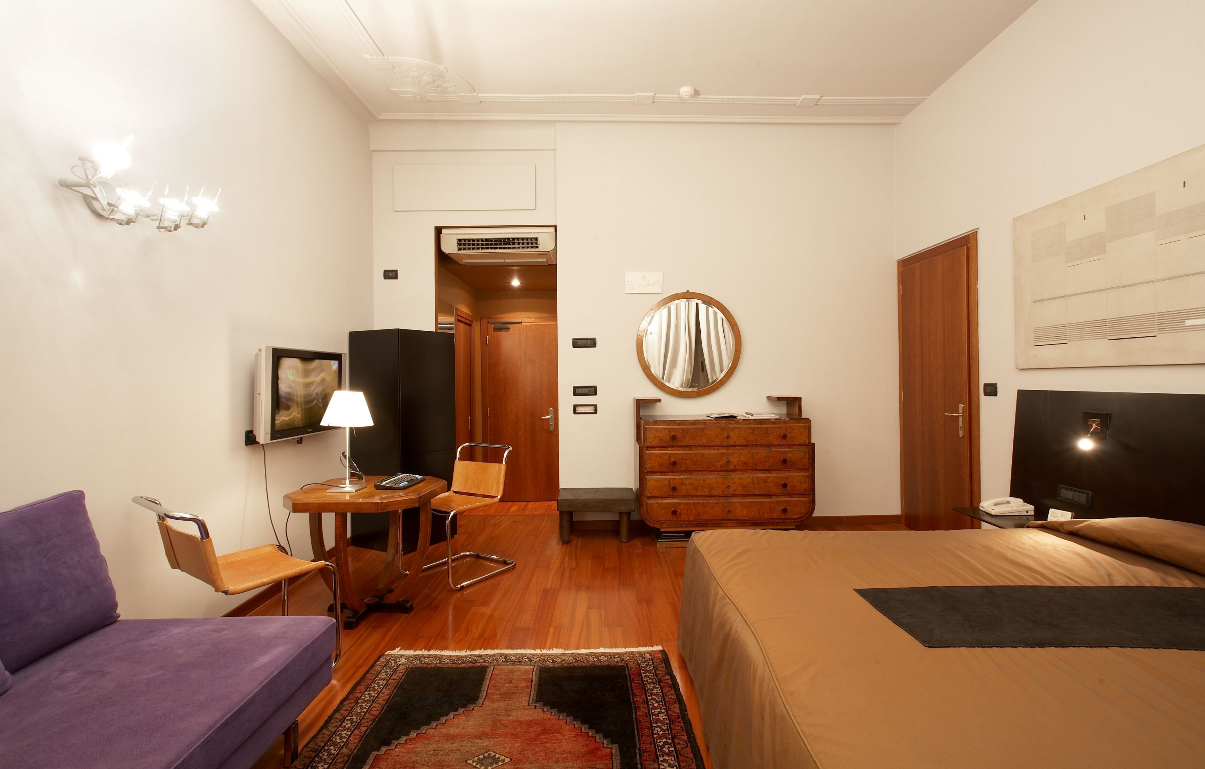 A hotel room with a bed, a desk with a chair, a sofa, a dresser, a mirror, and a television.