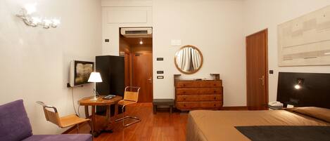 A hotel room with a bed, a desk with a chair, a sofa, a dresser, a mirror, and a television.