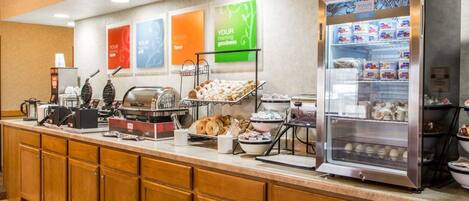 A breakfast bar with a coffee machine, waffle maker, and various food items.