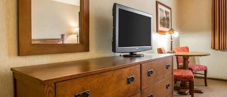 A hotel room with a wooden dresser, a television, a framed picture on the wall, and a red chair.