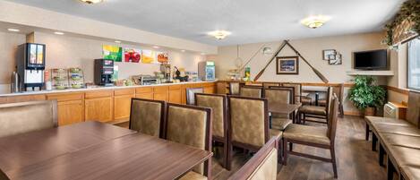 A restaurant with wooden tables and chairs, a counter with a beverage dispenser, and a TV mounted on the wall.