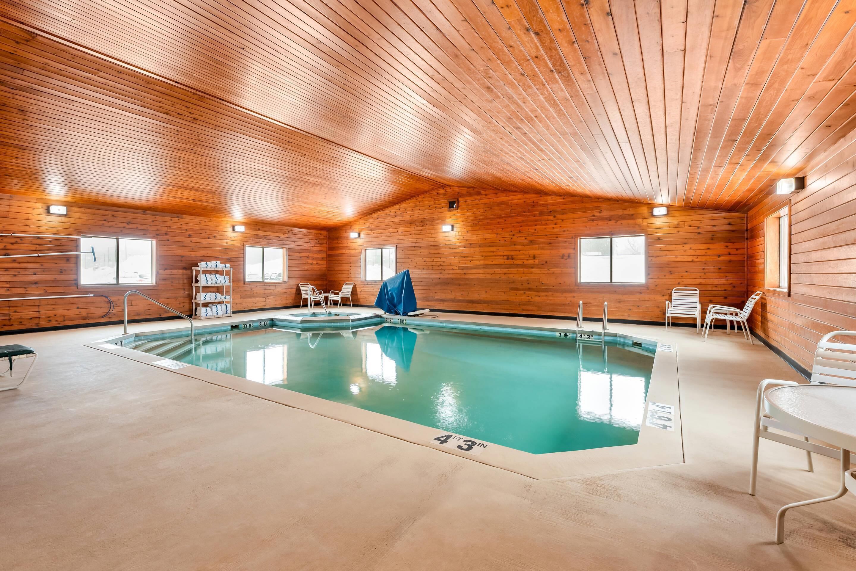 Una piscina interior con paredes y techo de madera, marcas claras en la piscina y algunas sillas.