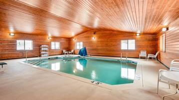 An indoor swimming pool with wooden walls and ceiling, clear pool markings, and a few chairs.
