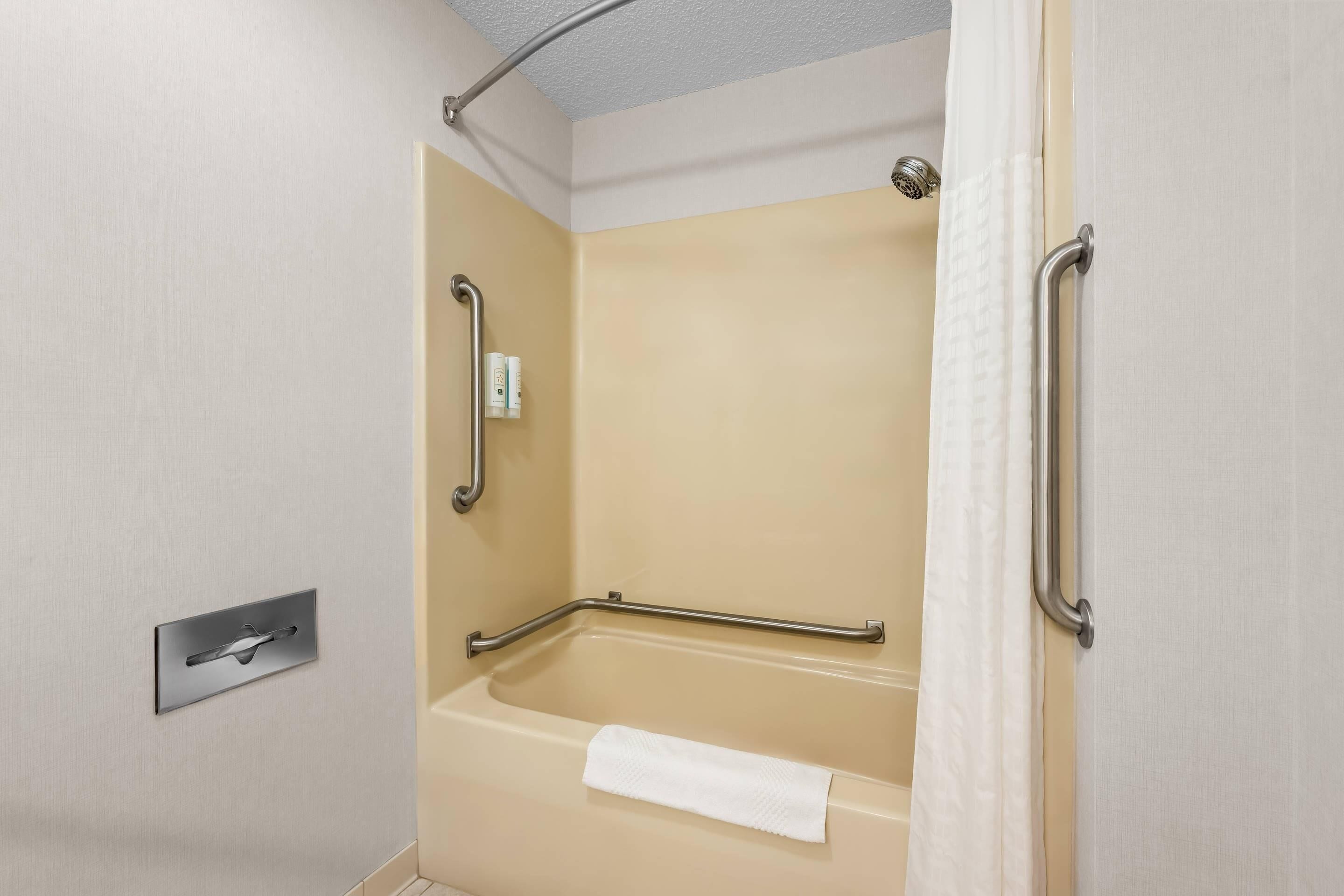 A shower with a grab bar, a towel, and a control panel.