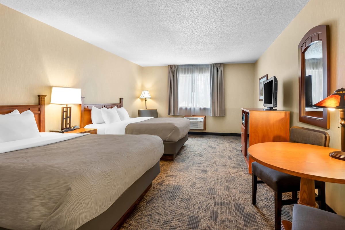 A hotel room with two beds, a desk, a chair, a television, and a mirror.