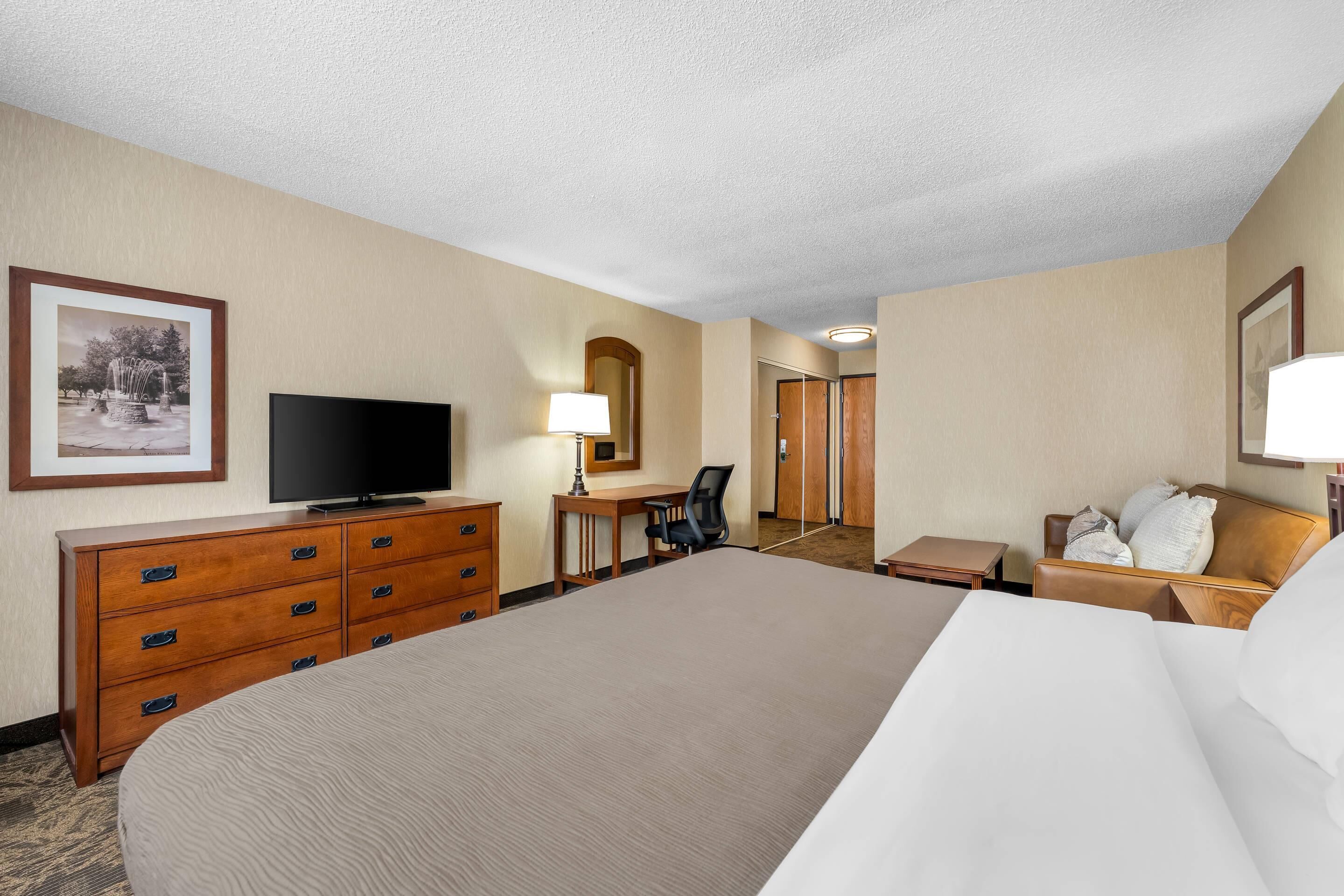 Une chambre d’hôtel avec un grand lit, un bureau avec une chaise, une télévision, une lampe et un tableau encadré au mur.