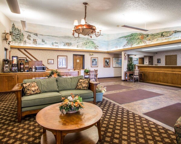 A lobby with a green sofa, a wooden coffee station, a reception desk, and a mural on the ceiling.
