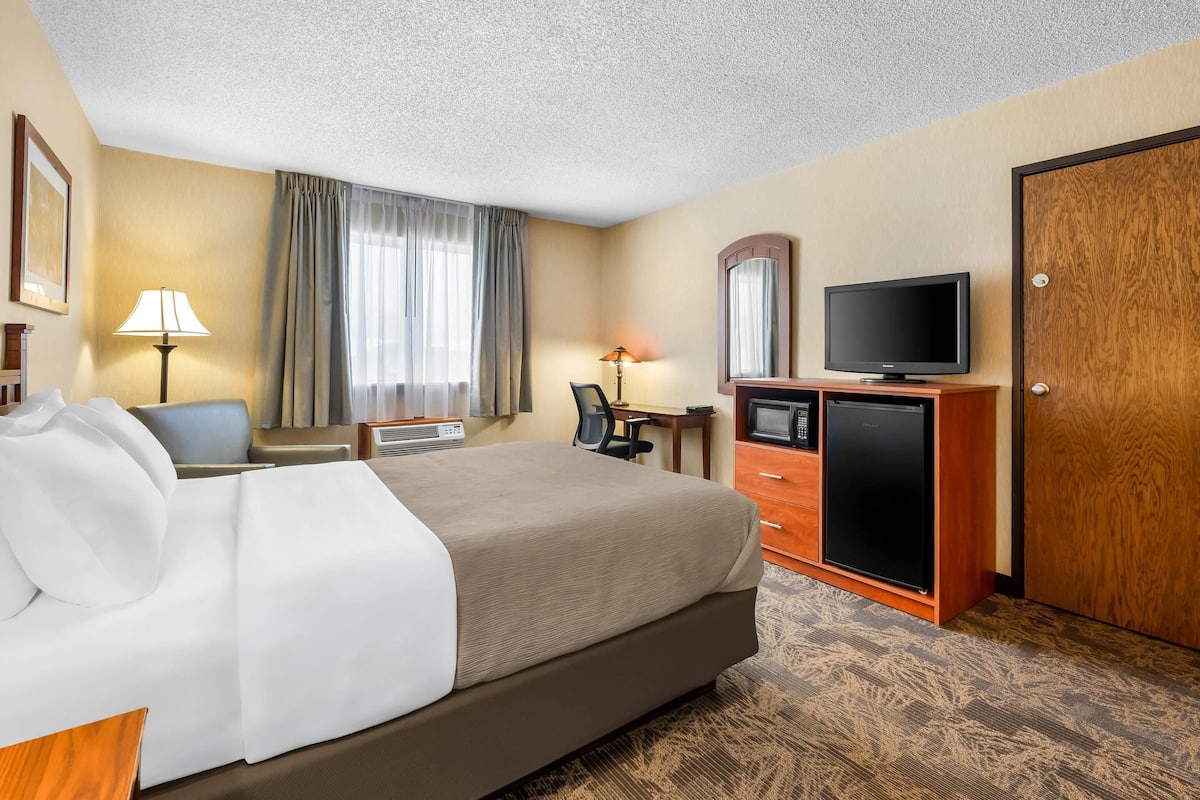 A hotel room with a bed, desk, television, and wardrobe.