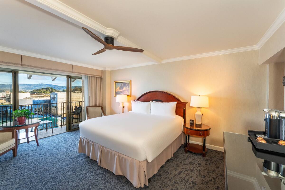 A hotel room with a large bed, a balcony with a view, a ceiling fan, and a coffee maker.