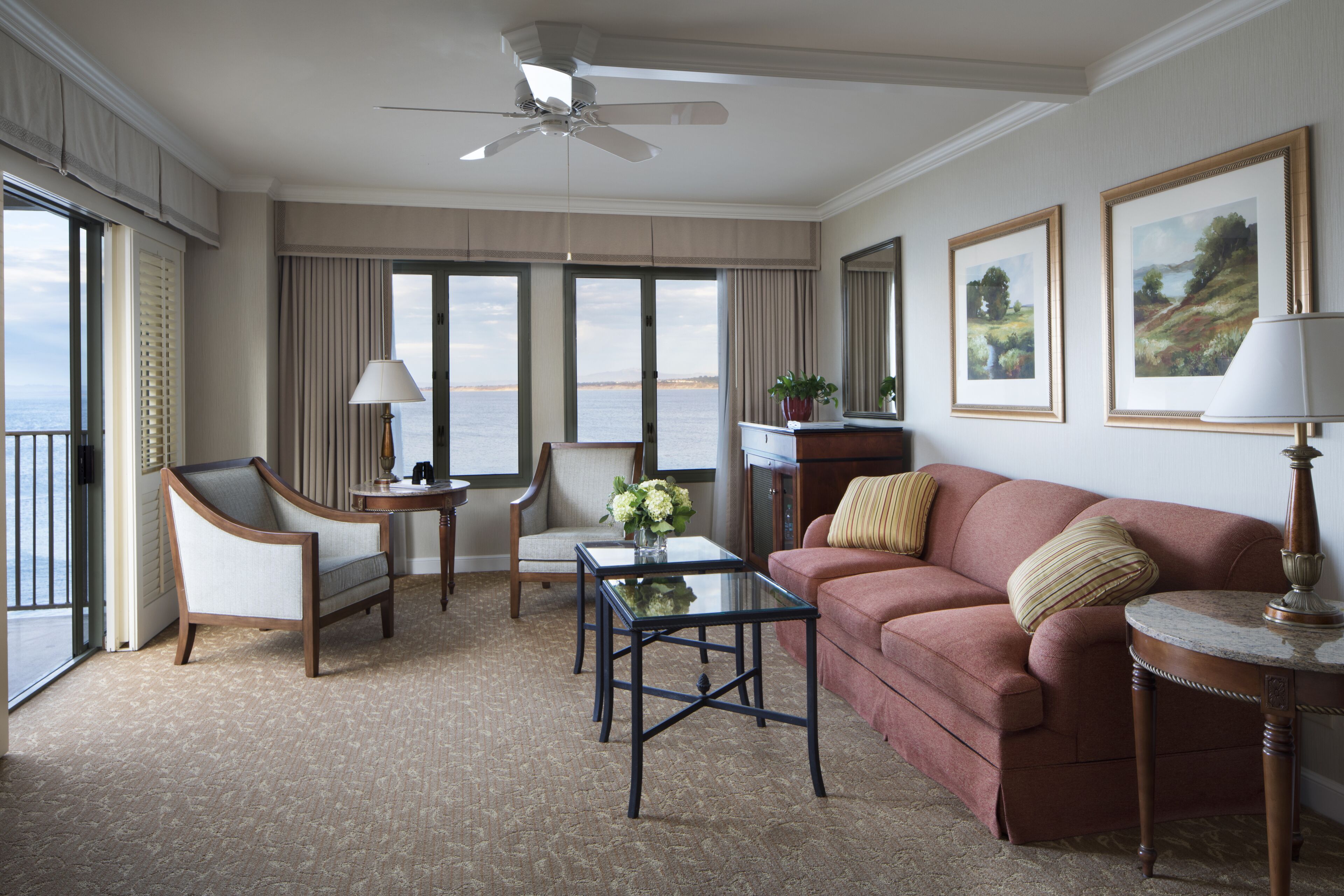 A hotel room with a large window, a ceiling fan, a sofa, a coffee table, and a chair.