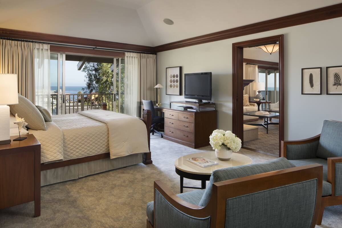 A hotel room with a bed, a desk, a chair, a TV, and a view of the ocean.