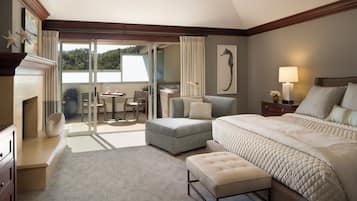 A bedroom with a large bed, a seating area with a table and chairs, a fireplace, and a view through a sliding glass door.