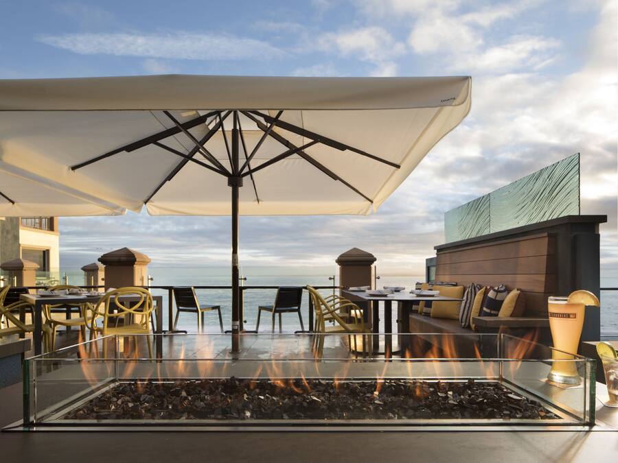 Un espace extérieur aménagé avec des sièges, une table basse surmontée d’un foyer en verre, des tables, des chaises et des parasols.