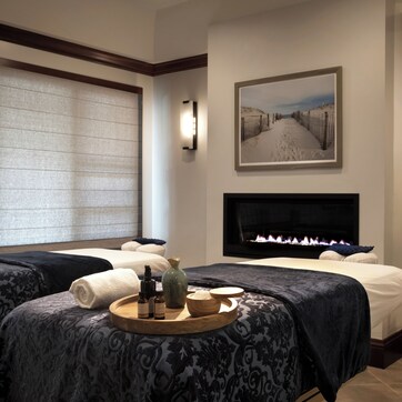 A hotel room with two beds, a fireplace, a painting, and a tray with amenities.