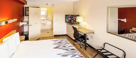 Habitación de hotel con cama, escritorio, silla y baño visible a través de una puerta abierta.