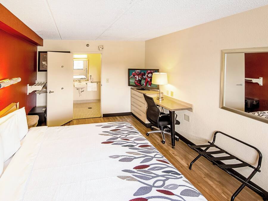 A hotel room with a bed, desk, chair, and a bathroom visible through an open door.