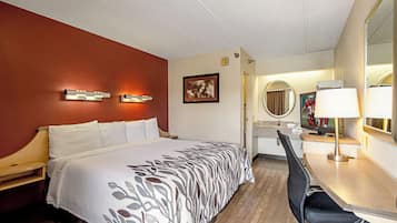 A hotel room with a bed, a desk with a chair, a mirror, and a television.