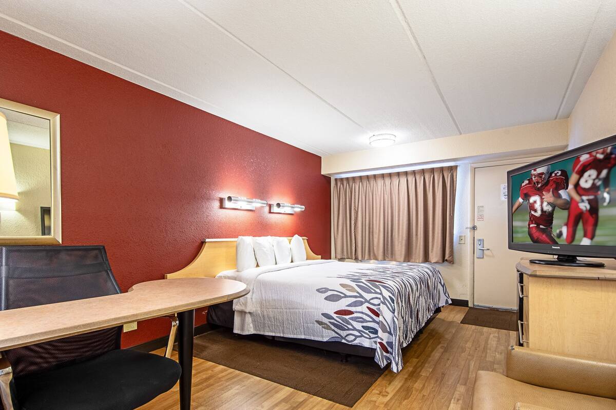 Une chambre d’hôtel équipée d’un lit, d’un bureau, d’une chaise, d’une télévision et d’une fenêtre avec des rideaux.