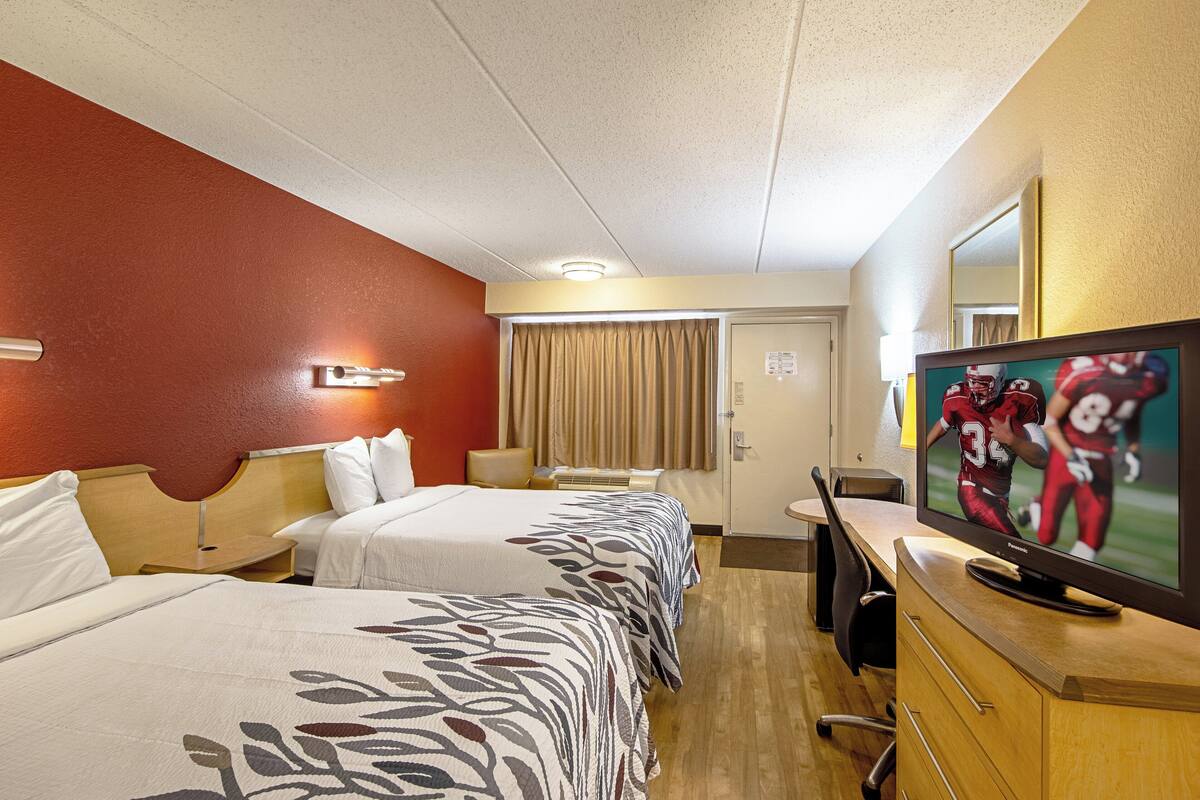 A hotel room with two beds, a television, a desk, and a mirror.