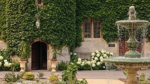 A building with a fountain in front, surrounded by a garden with white flowers and a paved walkway. - Thornbury Castle, Relais & Châteaux (Bristol)