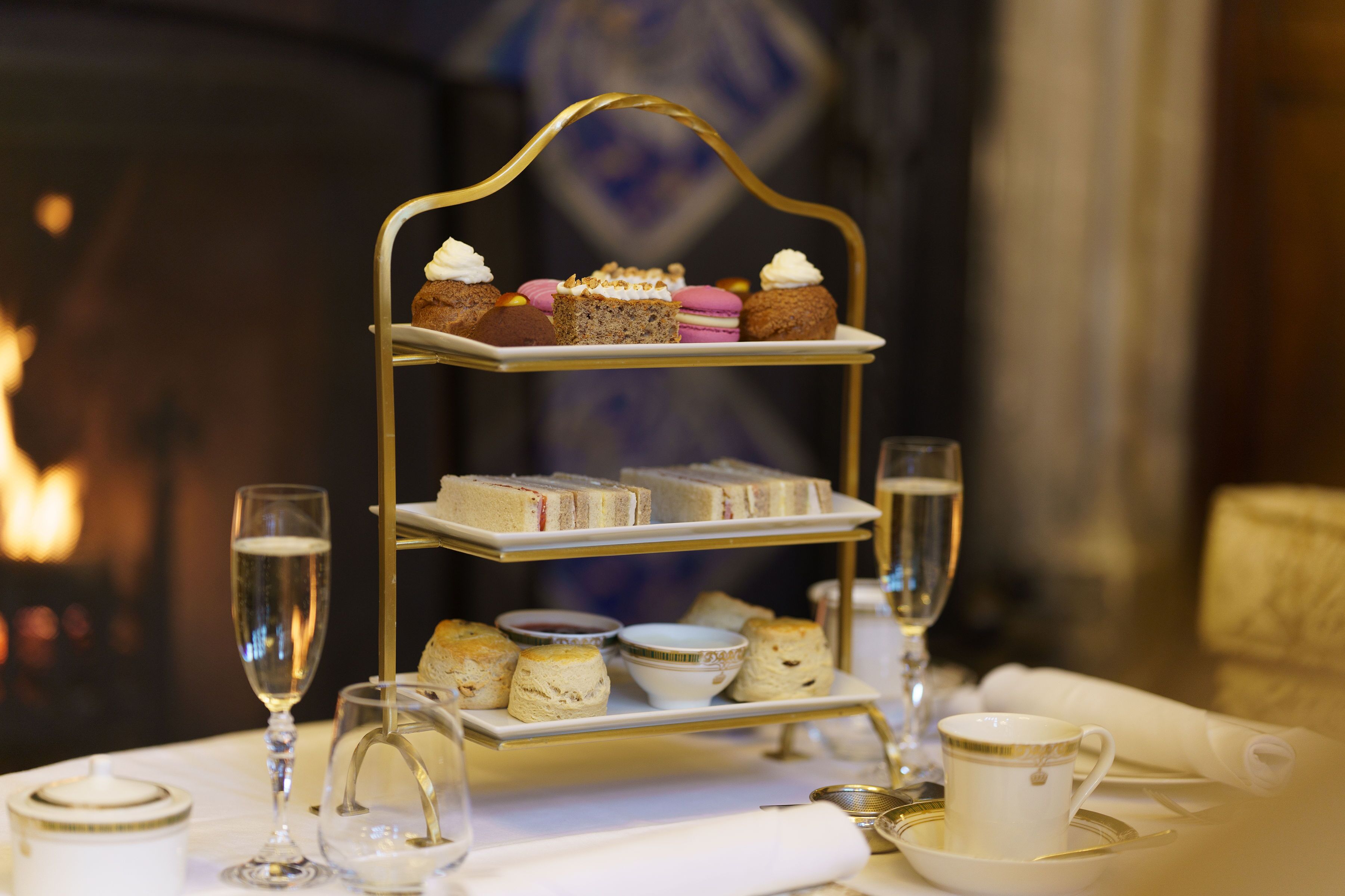 A tiered dessert stand with various pastries and scones, accompanied by tea cups and a glass of water on a table.