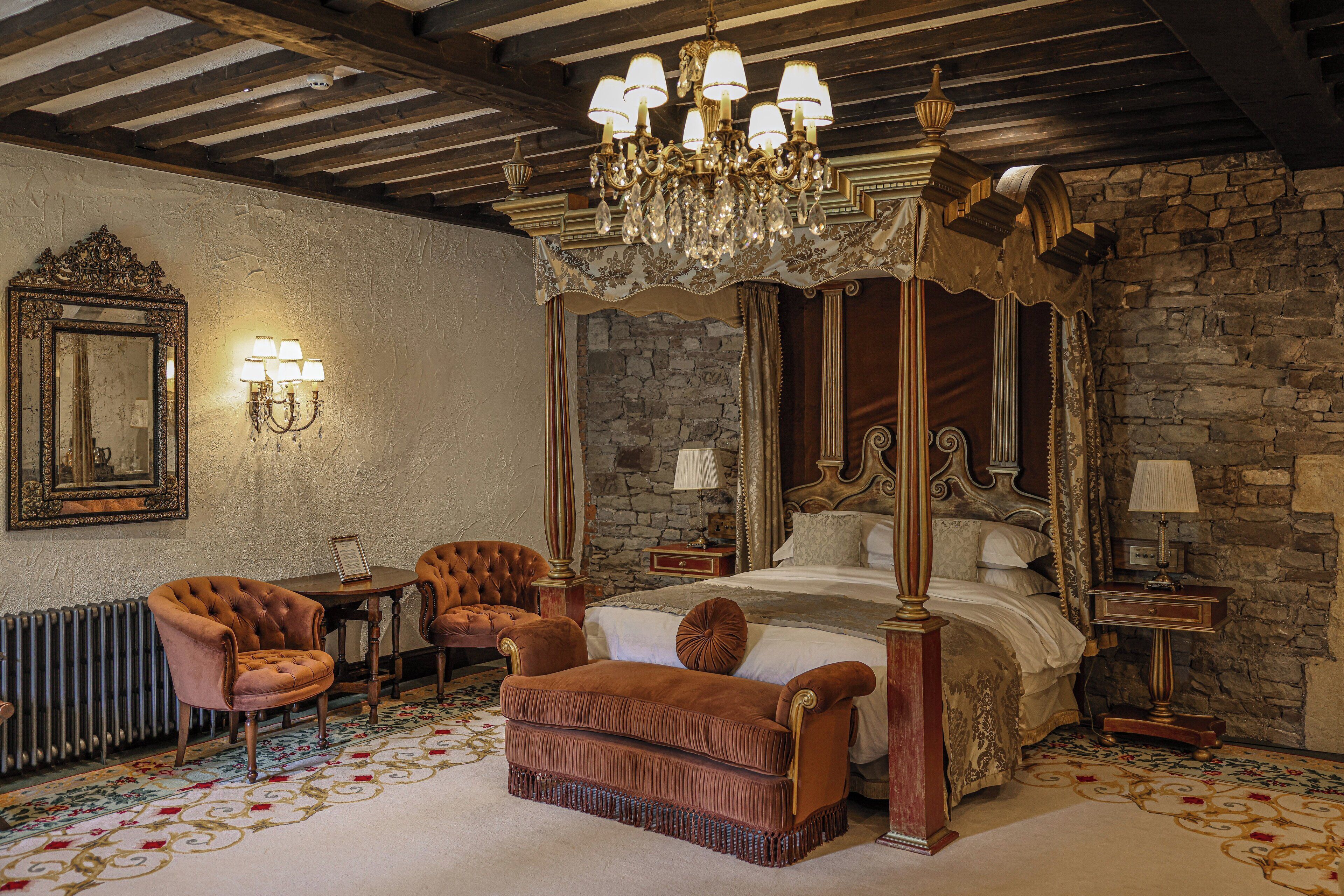 A four-poster bed with a canopy, a chandelier, and a stone wall.