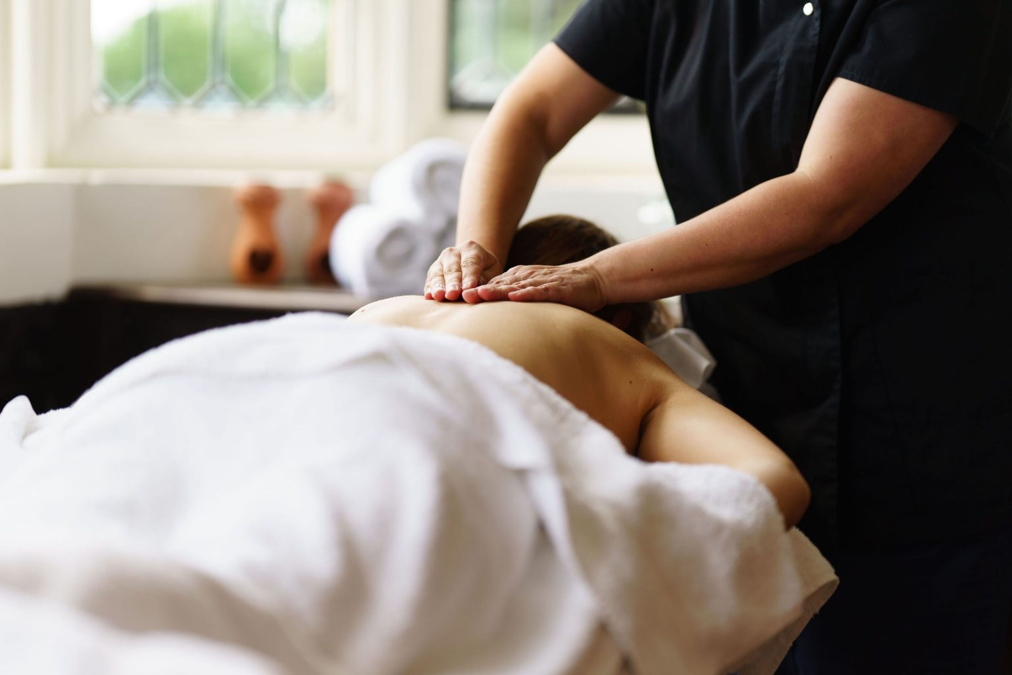 A person receiving a back massage in a room with a window and a towel rack in the background.