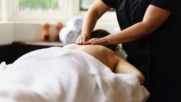 A person receiving a back massage in a room with a window and a towel rack in the background.