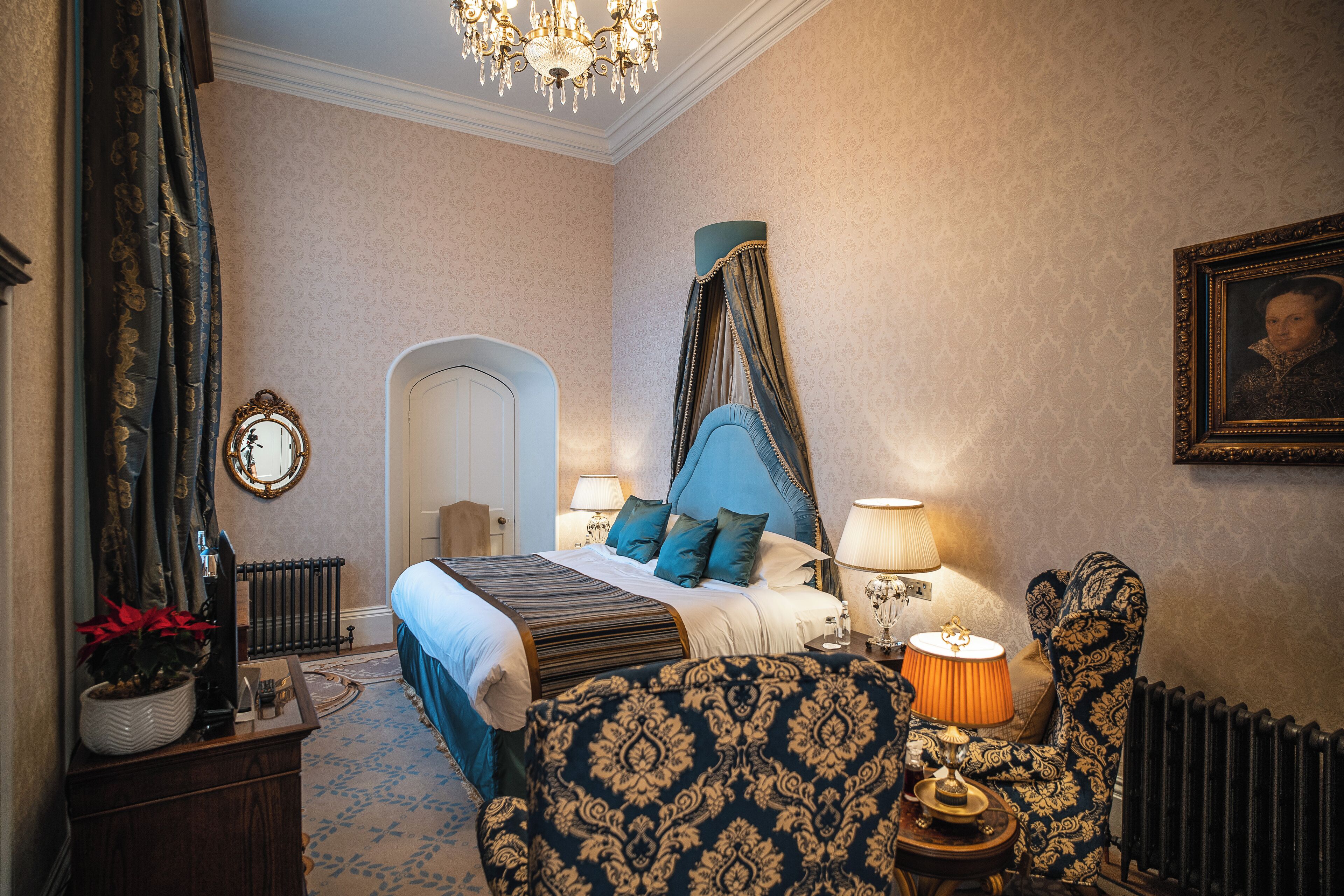 Ein Schlafzimmer mit einem Bett, Nachttischlampen, einem Sessel, einem Schminktisch, einem Spiegel und einer Chandelier.