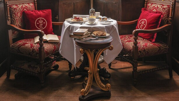A room with large arched windows, a chandelier, two ornate chairs with red cushions, and a table with a white tablecloth. - Thornbury Castle, Relais & Châteaux (Bristol)