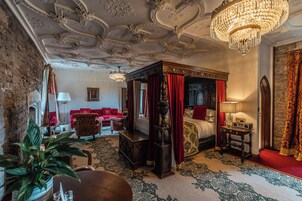 Um quarto luxuoso com cama de dossel, cortinas vermelhas e detalhes ornamentados no teto.
